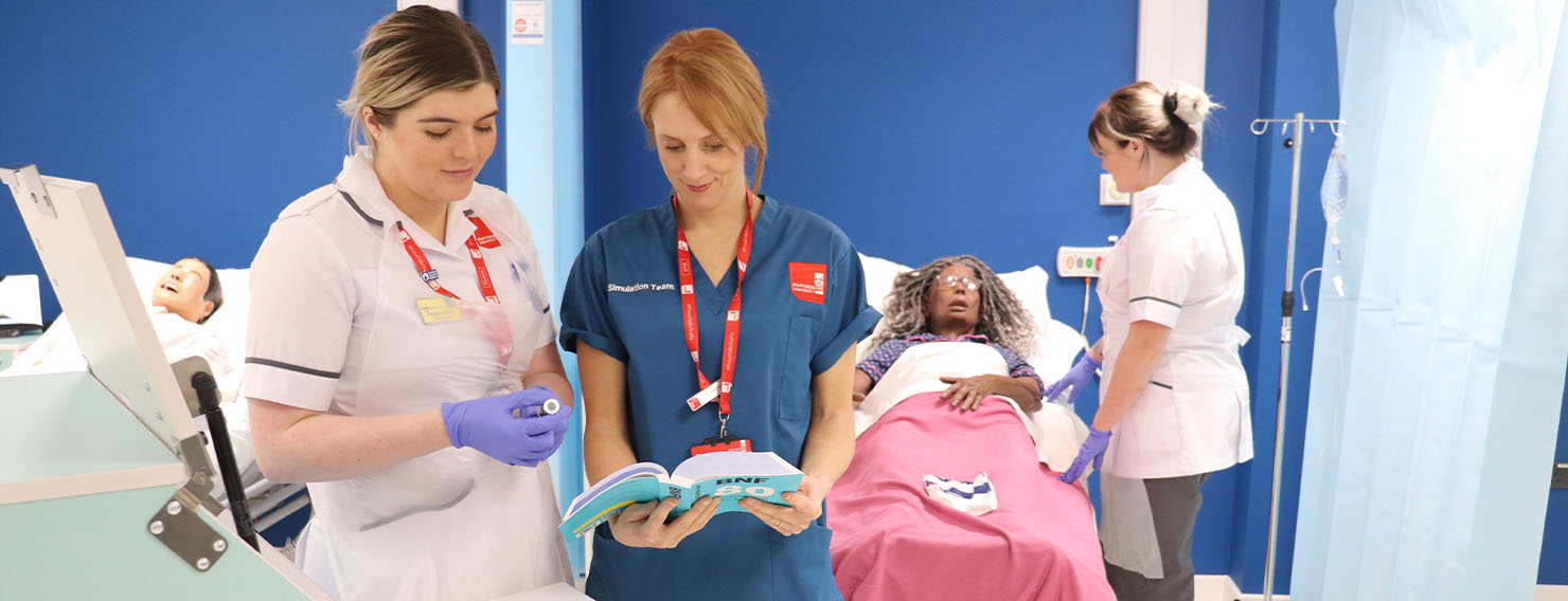 A nursing student with a technician looking at the British National Formulary in an adult ward simulation.