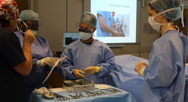 A group of apprentice operating department practitioners are wearing full surgery uniforms in a clinical simulation room