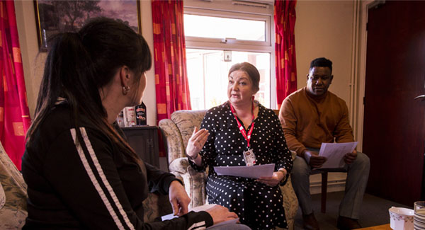 Three adults are sitting talking to one another in a living room social care visit setting