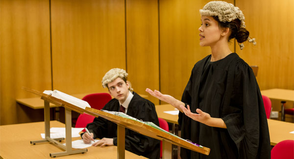 A female practicing law is wearing barrister clothing and standing up talking to an audience