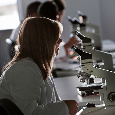 A female wearing a lab coat sitting in the science lab using a microscope