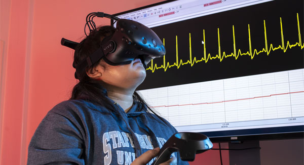 A student wearing a navy Staffordshire University hoodie using virtual reality equipment and a smart watch in the science lab