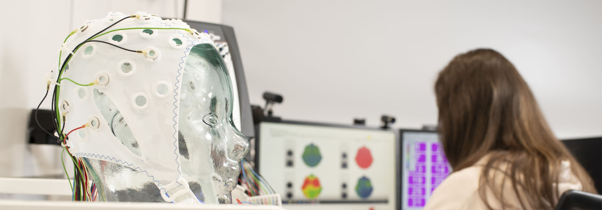 A female with brown hair is in the neuroscience lab analysing data and surrounded by electroencephalogram equipment