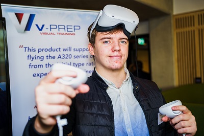 Male wearing VR headset and hand controls in front of company pull up banner.