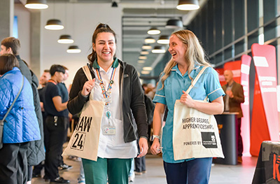 Two women smiling and holding at National Apprenticeship Week  tote bags