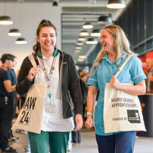 Two women smiling and holding at National Apprenticeship Week  tote bags