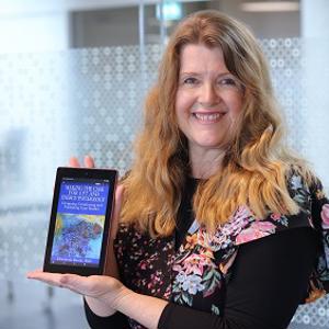 Professor Liz Boath pictured with a Kindle displaying her book