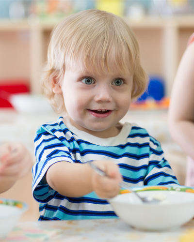 A child with fair hair is sitting at a table with a bowl