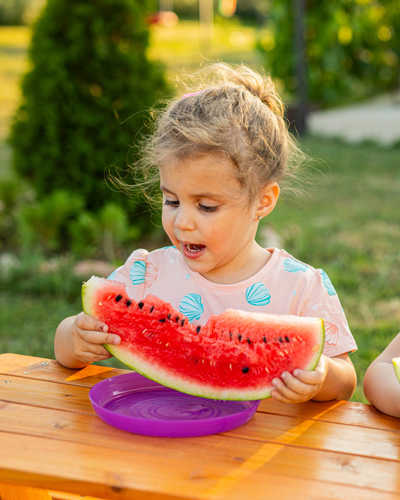 A young girl is sitting outside eating a slice of watermelon