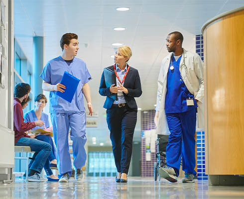 Medical professionals walking through a corridor, two are wearing scrubs and another is dressed in a smart business suit
