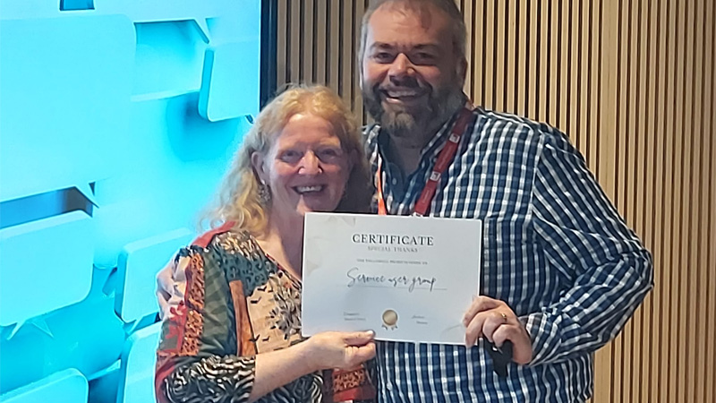 Two service users are attending an awards ceremony, holding an award and smiling for a photo