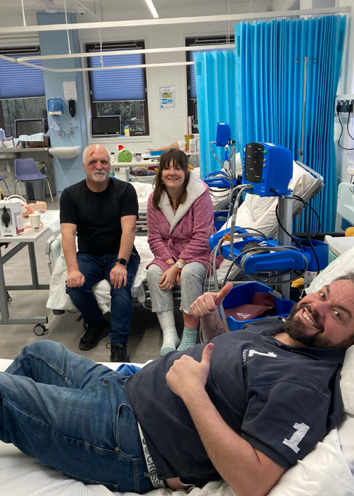 Three service users are taking part in a nursing simulation, a man is lying on a bed