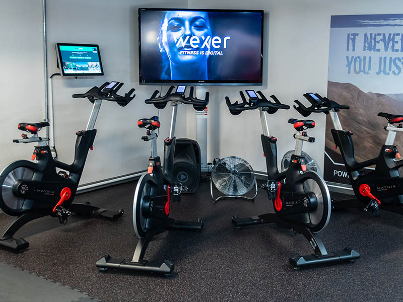 row of spin bikes in front of screen featuring Wexer Virtual Fitness