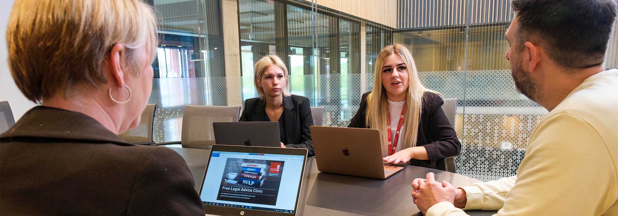 Male client receiving legal advice from two female law students, they are accompanied by a solicitor in a bright office.