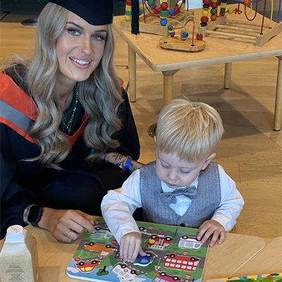 A female student wearing graduation attire is with her child in the nursery