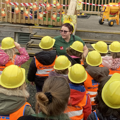 A group of children are wearing hard hats in the garden with a teacher
