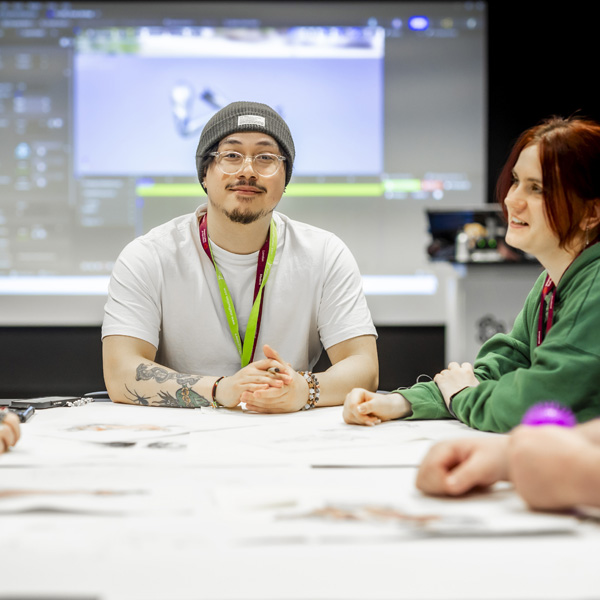 Gaming students are gathered around a large table collaborating on projects