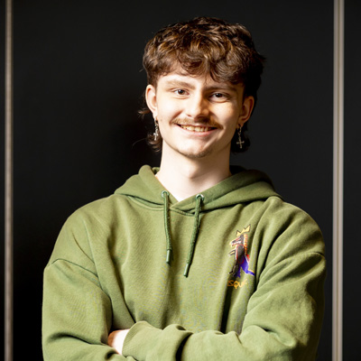 A young male student wearing a green hoodie is smiling for a photo