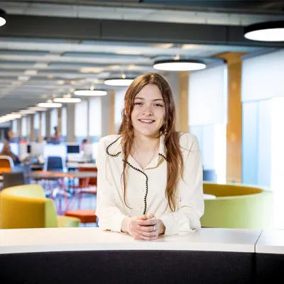 A female with long brown hair wearing a white blouse is in the Catalyst building