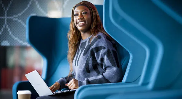 A female with long hair is smiling using a laptop