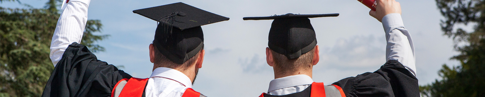 Two graduates in full dress holding their certificate scrolls aloft