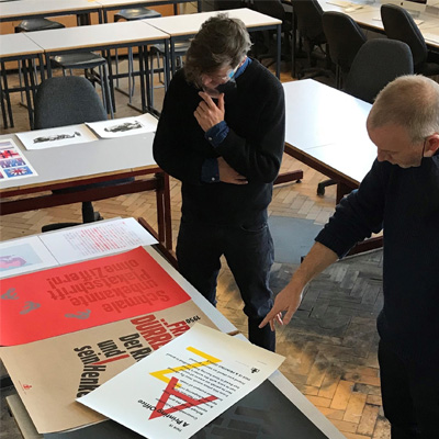 Ed and joe are in the seminar room discussing various materials of print laid out on the table