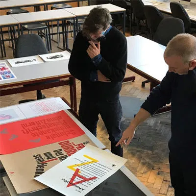 Ed and joe are in the seminar room discussing various materials of print laid out on the table