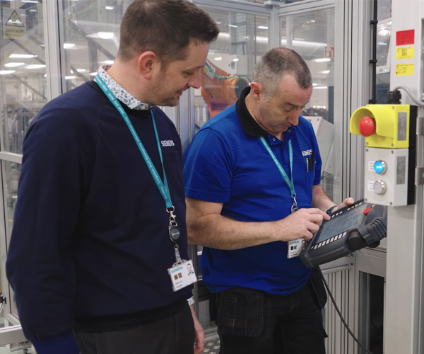 Two male staff members wearing uniform shirts are in the lab working together
