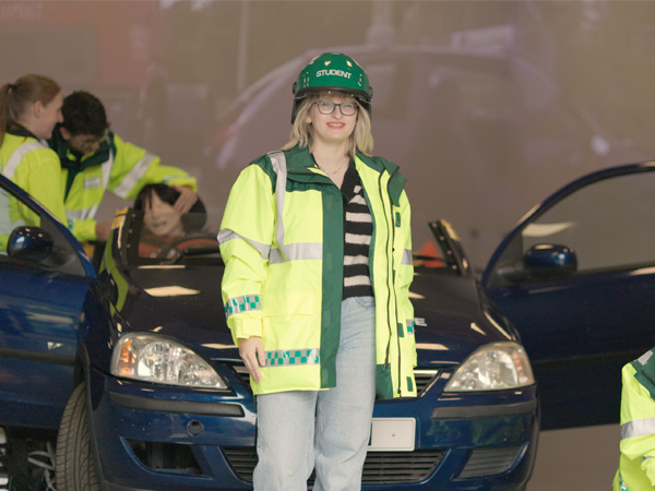 A female student wearing a students emergency response uniform is standing in the simmersive suite. Other students in the background are taking part in a simulation.