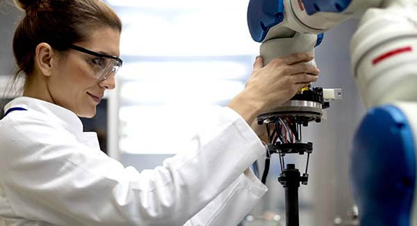 female engineer uses a machine in the lab, she is wearing safety goggles and a white lab coat