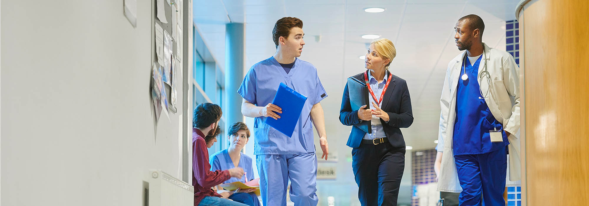 three healthcare professionals walking down a corridor, one is dressed in a smart business suit and the other two are wearing scrubs