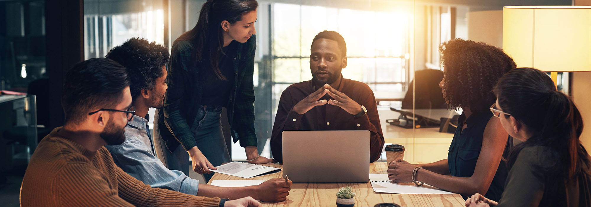 a multi-ethnic group of business men and women sit around a table discussing ideas.