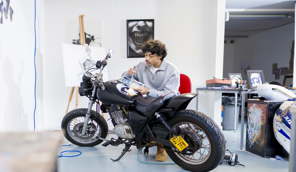 A young male student is working on a painted design on a motorbike in the fine art studio