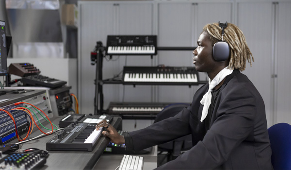 A male student wearing headphone is using the music technology equipment and keyboard in the lab