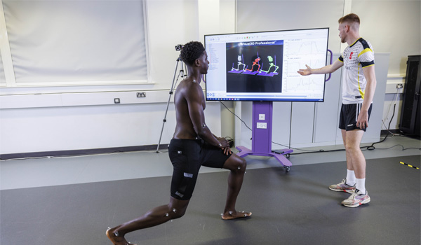 Two males are in the sports physiology lab testing body movements and monitoring on a screen