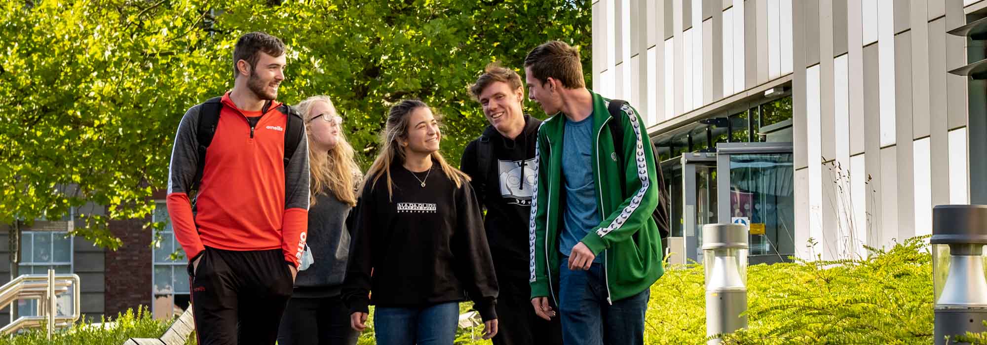 Group of mixed students walking past the Beacon building on College Road, it is a bright day and they are all wearing brightly coloured clothing.