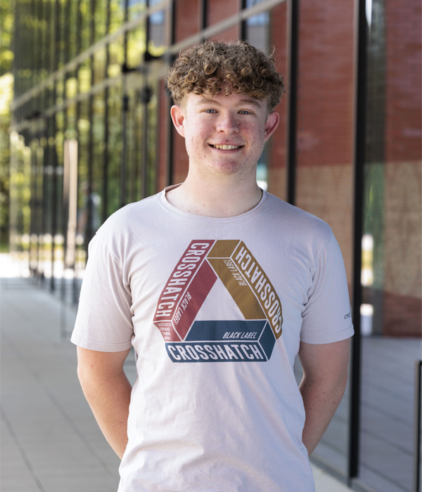 Headshot photoshoot of masters student Danny Rogers, who is smiling and wearing a white graphic tshirt
