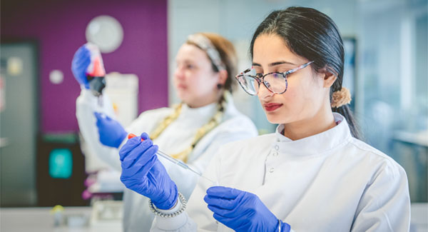 Female students wearing white forensics clothing and purple gloves testing substances in the science lab