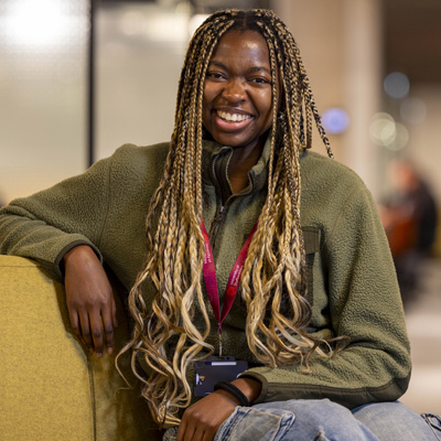 A female with long braids wearing casual clothing is sitting relaxed smiling