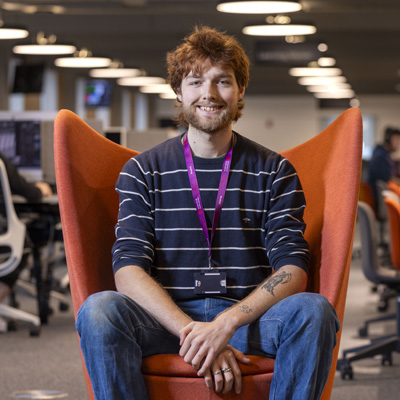 A male with a beard is smiling, sitting confidently in an orange chair