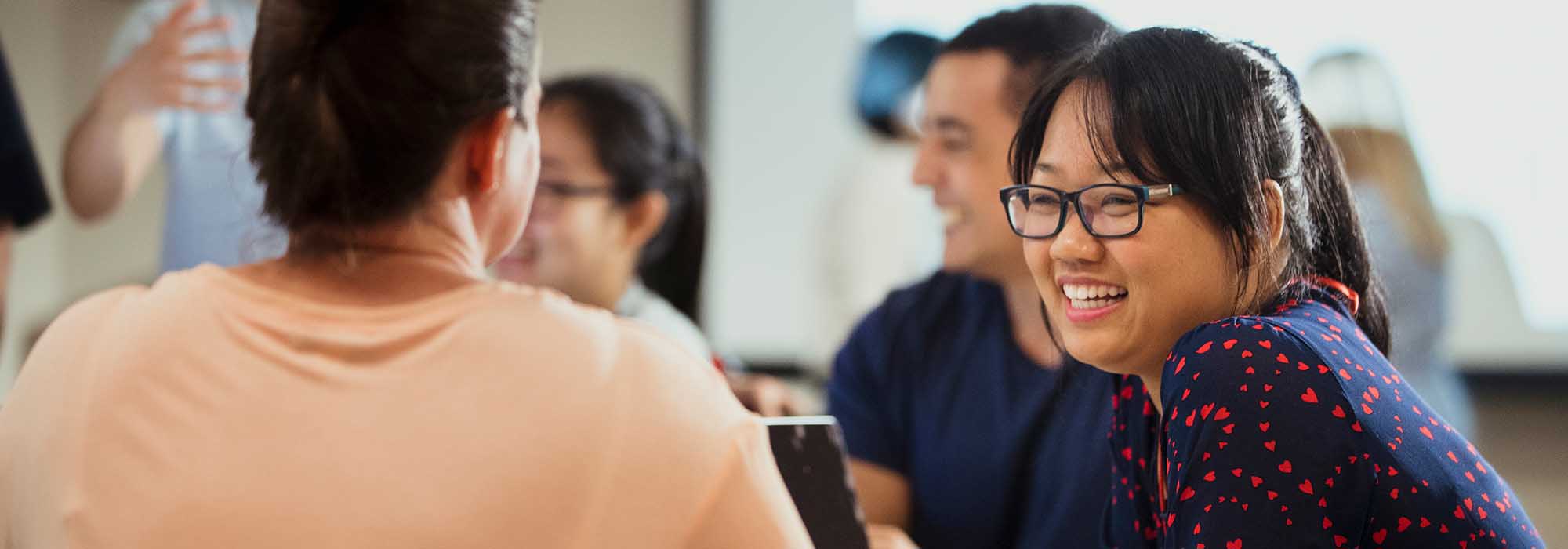 two female employees chatting in an office, one has a laptop.