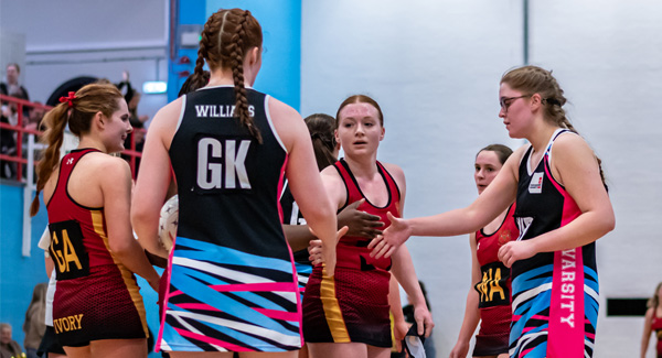 A team of female netball players are shaking hands in the sports hall