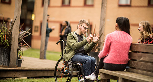male wheelchair user chatting to two female students in the gardens at Clarice Cliff accommodation
