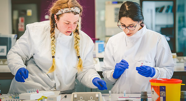 two female biomedical science students wearing lab coats and gloves working in our science centre