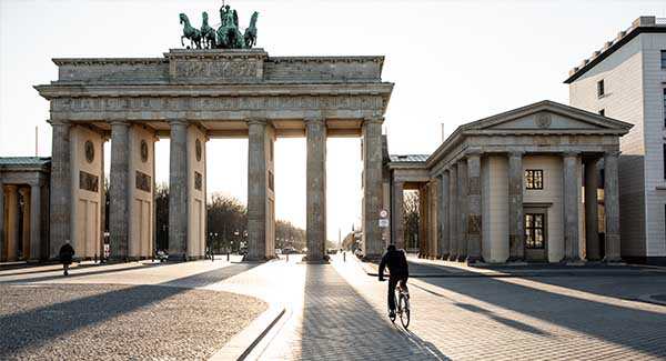 A cyclist rides past as sunlight beams through the Bradenburg Gate in Berlin.