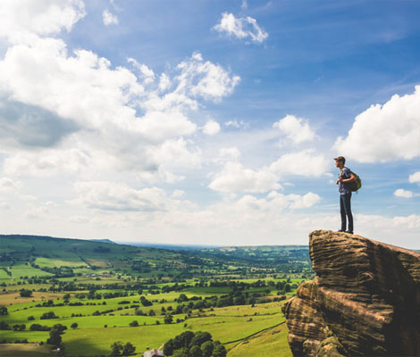 A male hiker standing on top of a rock taking in the scenic peak district view on a sunny day