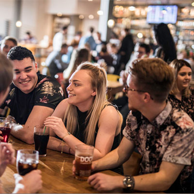 A group of students sitting in a pub drinking and socialising with the bar behind them