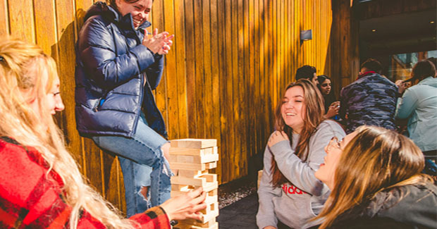 A group of female students wearing coats socialising outside the Verve playing jenga
