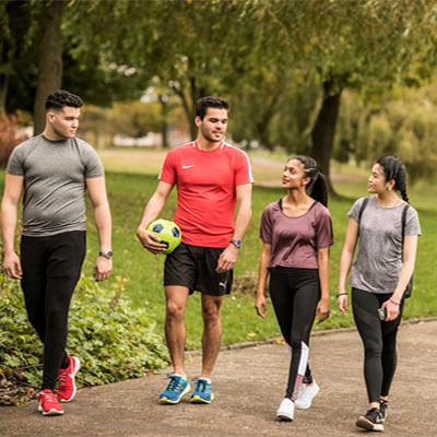 Group of four students dressed in active clothing walking in a park carrying a football