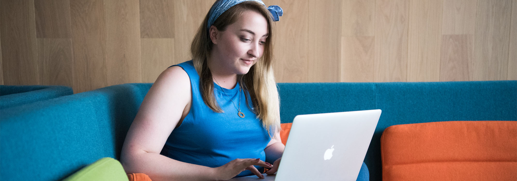 A female student wearing blue sitting cross-legged on the sofa using a laptop